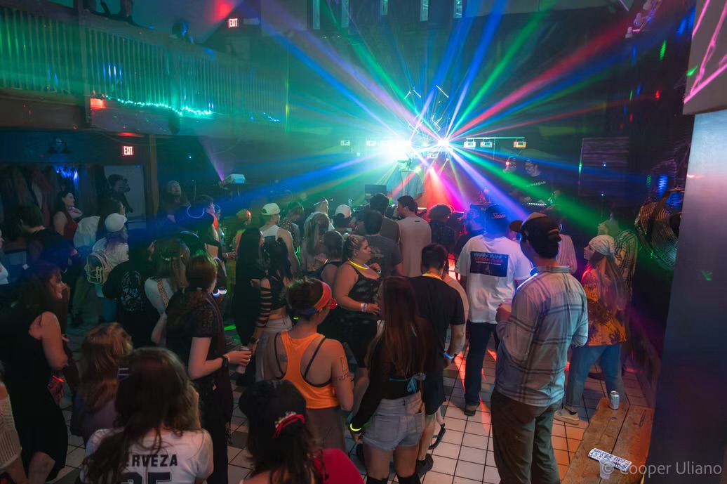 A packed dance floor under blue and green laser lights
